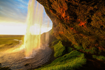 Fototapeta na wymiar Waterfall Selandjafoss Iceland at sunset or sunrise. Beautiful waterfall in Iceland. Golden hour. Cave and waterfall. Travel in Iceland. Beautiful sky against the big waterfall. inside the water. 