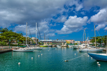Fototapeta na wymiar Bridgetown, Barbados - 22 Sept 2018: Sailing yachts moored in the downtown marina bay of Bridgetown, Barbados, Caribbean. White clouds in the blue sky. Copy space