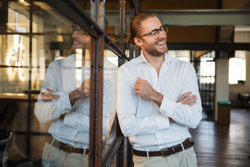 Photo of joyful caucasian man laughing while leaning on glass wall