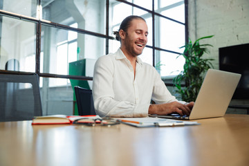 Photo of handsome laughing man working with laptop while sitting