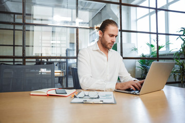 Photo of handsome thinking man working with laptop while sitting
