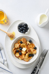 Tiny cereal pancakes with blueberry and honey on white background. View from above.