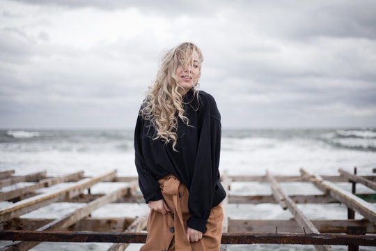 Beautiful young girl on a background of the sea. Blonde portrait photo. Autumn, cloudy weather, the sea is raging
