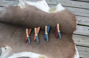 A set of four fixed blade damascus hunting knives displayed on deer hide on a wooden deck with...