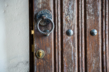 Close up on rusty metallic oriental style door knocker and golden key lock. Brown old wooden door. Vertical photo with copy space