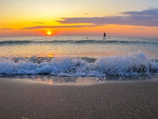 Stand up paddlers enjoy tropical island sunset in pacific ocean active couple stand up paddling together, sunset silhouettes. Boy nad girl enjoing on Paddle board on summer day. SUP exotic sunrise