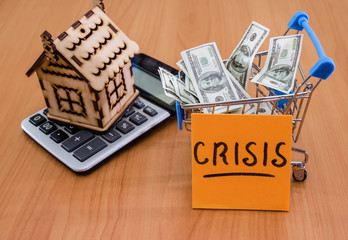 Crisis on a sticker on the background of a wooden house, a calculator and money. The problem is to buy or sell a house.