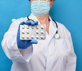 medic woman in white coat and blue latex gloves holds a pack of pills in a blister pack