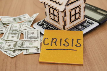 Crisis on a sticker on the background of a wooden house, a calculator and money. The problem is to buy or sell a house.