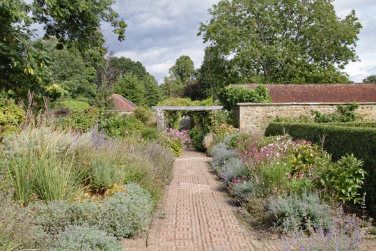 A brick path runs between abundant flower beds in an English country garden.