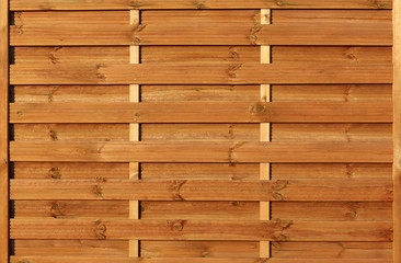 Bright orange wooden fence flooded with sunlight. One block of horizontal wooden panels with knots. For abstract wooden backgrounds and textures.