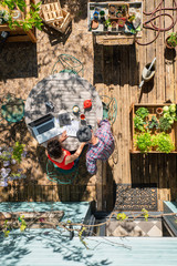 Top view, a couple uses a laptop computer on an outdoor table to find gardening tips for plants in wooden planters.
