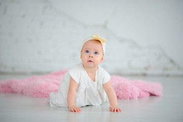 Little cute girl with big blue eyes. The girl is dressed in a white dress. Girl learning to crawl.