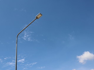 The lamp illuminates the street at night, looks like a tall pole, the background is a bright sky
