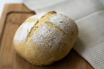 A loaf of homemade sourdough yeast bread boule with a simple cross style scoring technique on a wooden board. Dark and moody style.