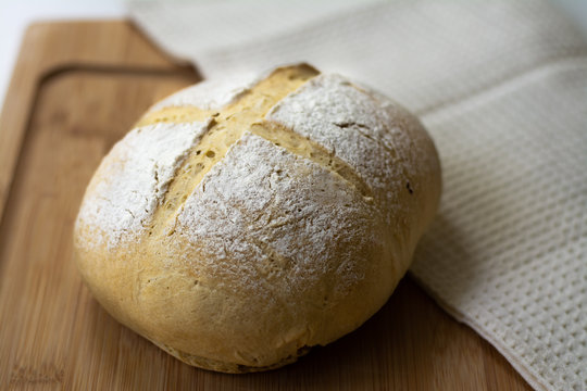 A loaf of homemade sourdough yeast bread boule with a simple cross style scoring technique on a wooden board. Dark and moody style.