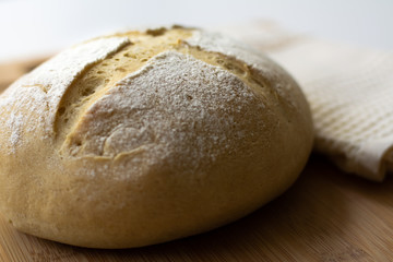 A loaf of homemade sourdough yeast bread boule with a simple cross style scoring technique on a wooden board. Dark and moody style.