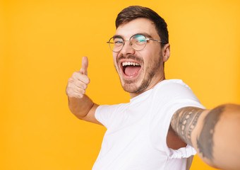 Photo of joyful young man taking selfie photo and showing thumb up