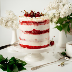 Red berry cake decorated with cherry berries and white cream, among lilac flowers and green leaves. Food photography. Advertising and commercial design.