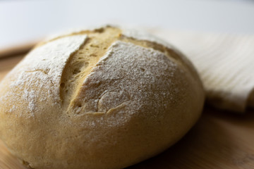 A loaf of homemade sourdough yeast bread boule with a simple cross style scoring technique on a wooden board. Dark and moody style.