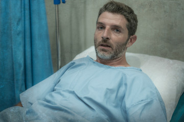 healthcare and medical - attractive worried and scared man in patient gown receiving treatment at hospital ward lying on bed feeling unwell and stressed in medicine concept