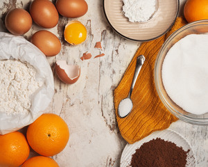 Ingredients to make an orange cake with eggs and chocolate on a wooden white background from above
