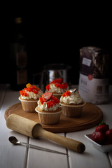 Cupcakes with cream and berries on a wooden tray