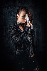 Young woman with scarified face, wearing a studded leather jacket, holding a revolver on her forehead