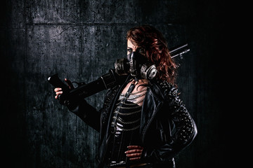 Naklejka premium Young woman with scarified face, wearing a studded leather jacket, gas mask, holding a shotgun in her hand