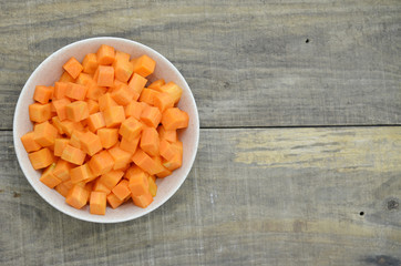 cuts cubes of carrot in bowl on wooden background