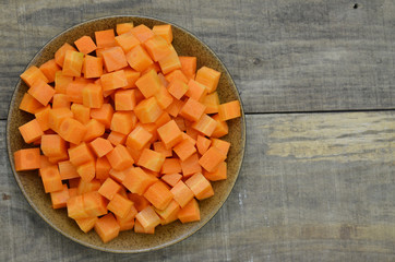 cuts cubes of carrot in black plate on wooden background