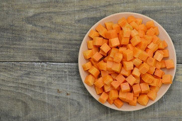 cuts cubes of carrot in white plate on wooden background