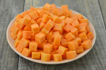 cuts cubes of carrot in white plate on wooden background