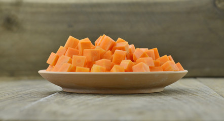 cuts cubes of carrot in white plate on wooden background