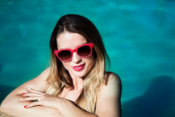 Portrait of a beautiful girl in pink glasses sunbathing in the pool.