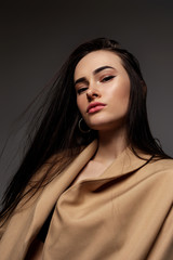 fashion brunette woman model with long hair in a beige pantsuit posing on studio background.