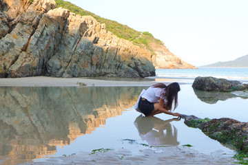 squatting girl by the sea, with water reflection