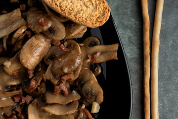 Cooked mushrroms with ham pieces on a black plate