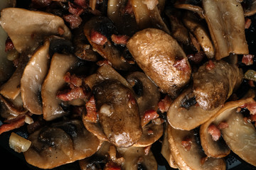 Cooked mushrroms with ham pieces on a black plate