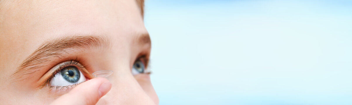 Little girl child putting contact lens into her eye isolated on a blue background