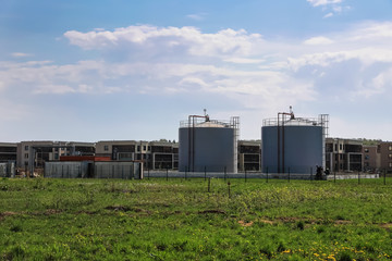 Industrial zone in a residential area. Water intake station with high pipes against the background of residential buildings, fields and sky.