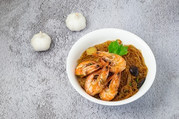 Casseroled shrimps roasted with glass noodles or prawns with Vermicelli Noodles in white blow with chinese celary on the top view. Asian Food Thai fusion style. famous food in Thailand national dish.