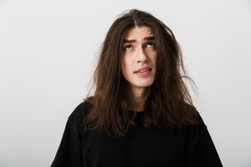 Portrait of handsome confused man with long hair poising and looking upward at copyspace