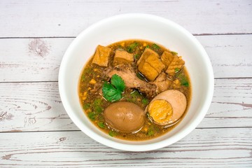  Stewed Drumstick chickens and half Egg with tofu,shiitake mushrooms in white bowl on wooden table in Thailand it call “Kai Palo”. famous Chinese & Asia food. National Thai dishes.