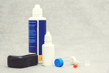 Rigid lens in silicone holder with liquid, container, cleanser, box and sucker on light background