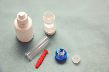Rigid lens in silicone holder with liquid, container, cleanser and sucker on light background