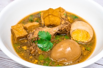  Stewed Drumstick chickens and half Egg with tofu,shiitake mushrooms in white bowl on wooden table in Thailand it call “Kai Palo”. famous Chinese & Asia food. National Thai dishes