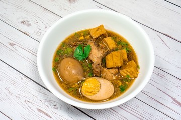  Stewed Drumstick chickens and half Egg with tofu,shiitake mushrooms in white bowl on wooden table in Thailand it call “Kai Palo”. famous Chinese & Asia food. National Thai dishes