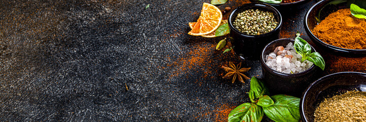 Set of Spices and herbs for cooking. Small bowls with colorful  seasonings and spices - basil, pepper, saffron, salt, paprika, turmeric. On black stone table top view copy space