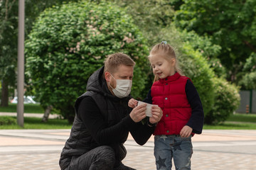 Little blonde girl with her father in medical masks in the park